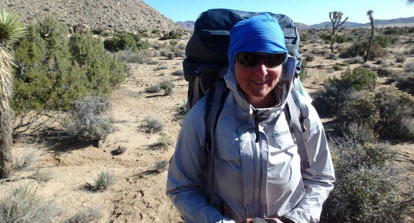 A person wearing a backpack smiles while standing in a desert. 